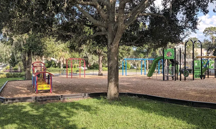 Área de recreação do Azalea Lane Playground em Winter Park, com árvores, escorregadores e balanços para crianças