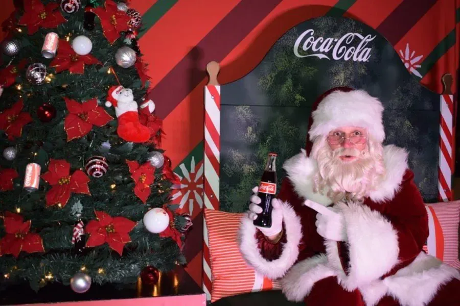 Papai Noel sentado ao lado de uma árvore de Natal segura e aponta para uma garrafa de Coca-Cola durante caravana que passa pela Flórida