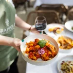 Garçom carrega prato de nhoque e taça de vinho durante festival gastronômico de Orlando em 2025