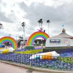 Escultura com arco-íris e bisnaga de tinta ao lado de um banner do EPCOT International Festival of the Arts da Disney