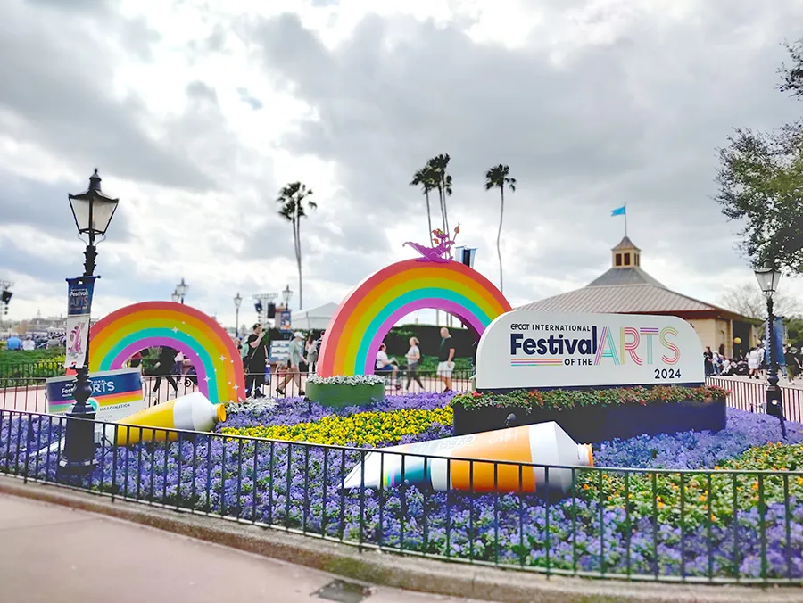 Escultura com arco-íris e bisnaga de tinta ao lado de um banner do EPCOT International Festival of the Arts da Disney