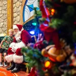 Papai Noel recebe criança no Disney Springs, com árvore de Natal à frente