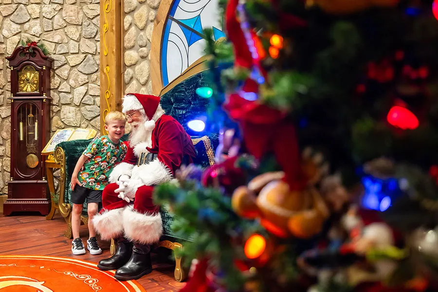 Papai Noel recebe criança no Disney Springs, com árvore de Natal à frente